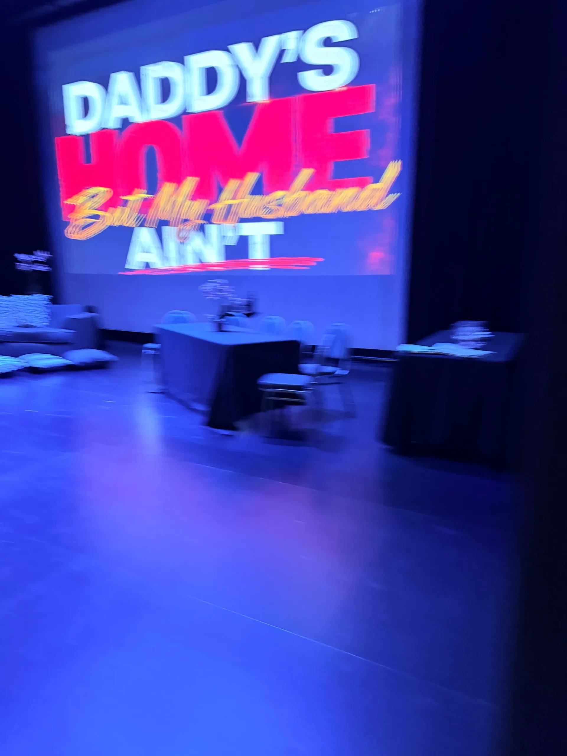 A theater screen displays the title Daddy’s Home But My Husband Ain’t above the stage
